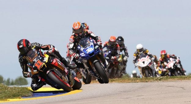 Mathew Scholtz (11) leads Jake Gagne (32) and the rest of the HONOS Superbike pack on the opening lap on Saturday. (Brian J. Nelson Photo)